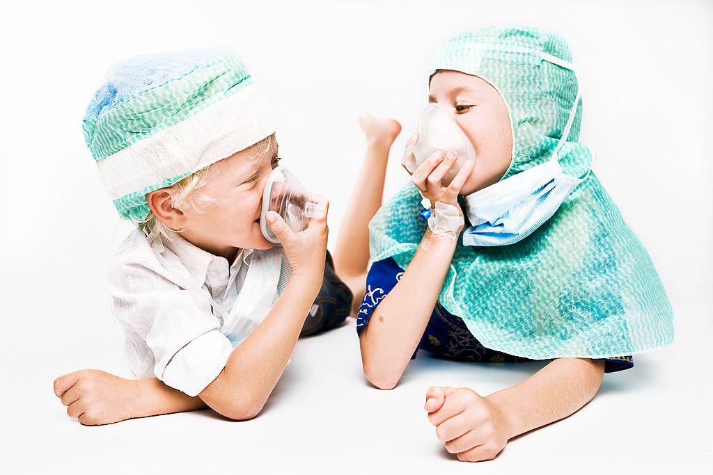 En flicka och en pojke i operationsmössor ligger på mage och andas i varsin syrgasmask.
