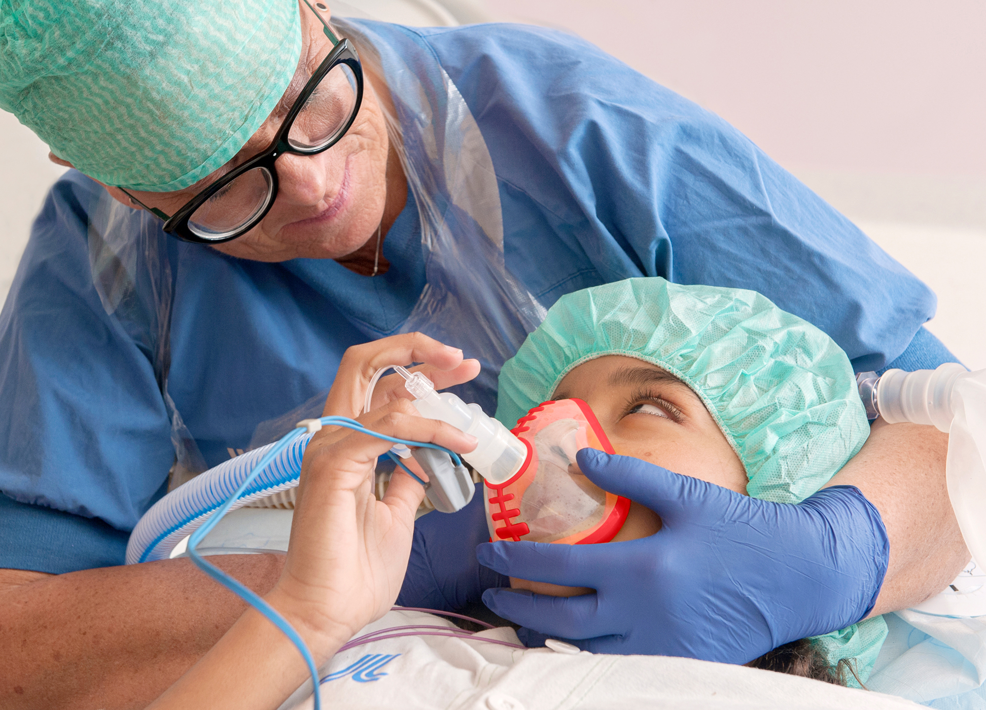 Sjuksköterska sitter bakom ett barn och håller en syretratt framför barnets näsa och mun. Barnet och sjuksköterskan tittar på varandra.