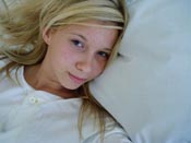 Blond tjej ligger i en säng med vita lakan