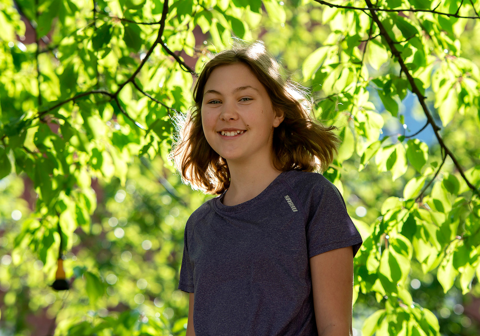 Mathilda, 14 år, ler mot oss med gröna träd i bakgrunden.
