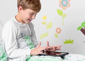 En pojke i en vit operationsskjorta sitter i en sjukhussäng och leker med sin Ipad.