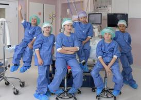 Flera barn i blå operationskläder sitter på ett operationsbord.