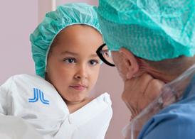 En flicka i en grön operationsmössa tittar djupt in i en sjuksköterskas ögon.