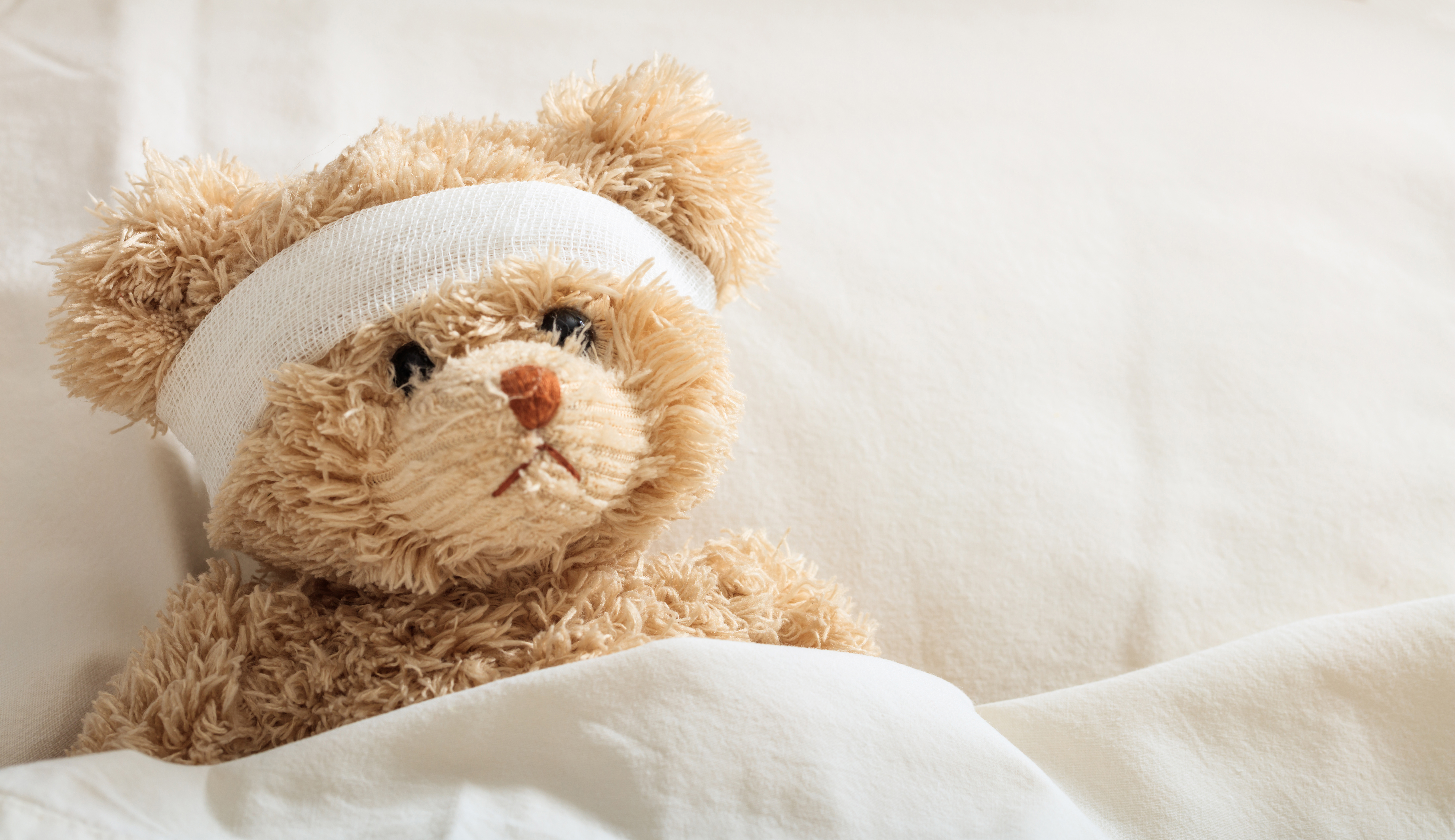 Nalle med bandage runt huvudet ligger i en säng.