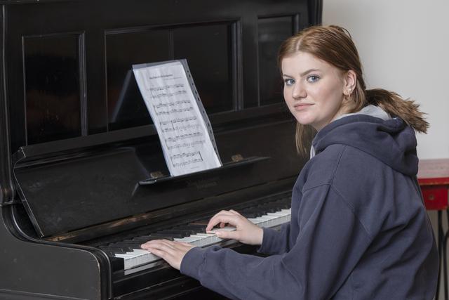 Tonårstjej i svart hoodie spelar piano