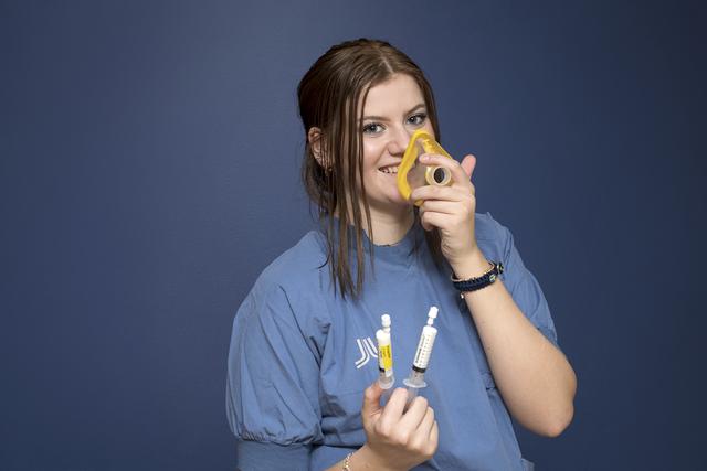 Tonårstjej i operationskläder. Hon håller två sprutor i en hand och andas i en sovtratt.