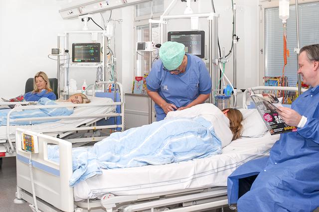 Två nyopererade patienter sover i sina sängar på uppvakningsavdelningen. En mamma och en pappa sitter bredvid sängarna.