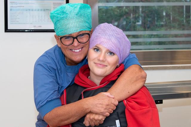 Tonårstjej i lila operationsmössa får en kram av en narkossjuksköterska.
