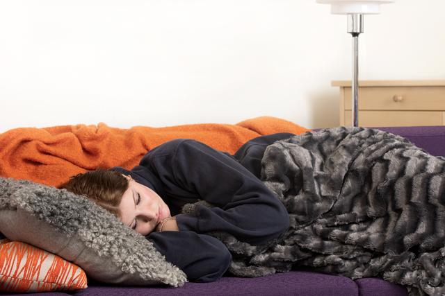 Tonårstjej ligger på en grå kudde i en orange soffa. Hon ser ledsen ut.